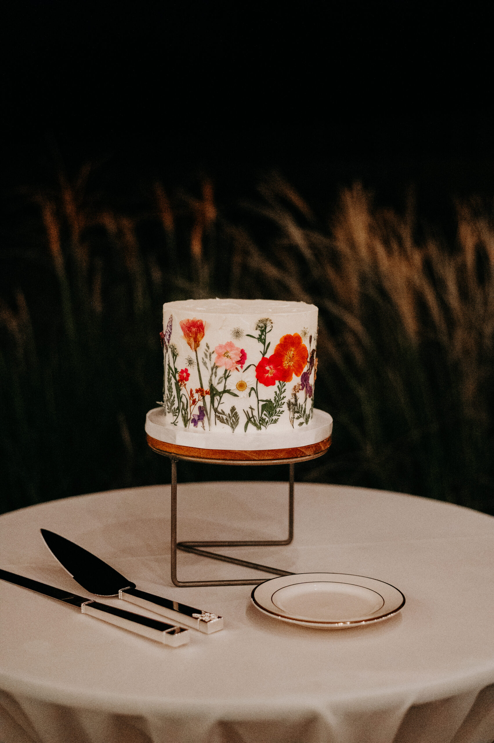 a wedding cake with dried pressed flowers with a cake cutting set and plate from a nashville wedding