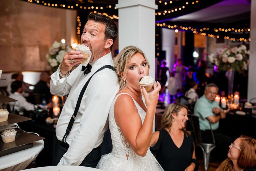 a bride and groom standing back to back eating cupcakes