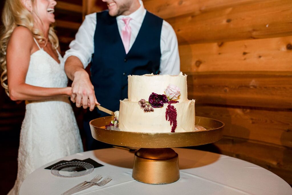 a two-tier wedding cake on a gold cake stand with a couple cutting it.